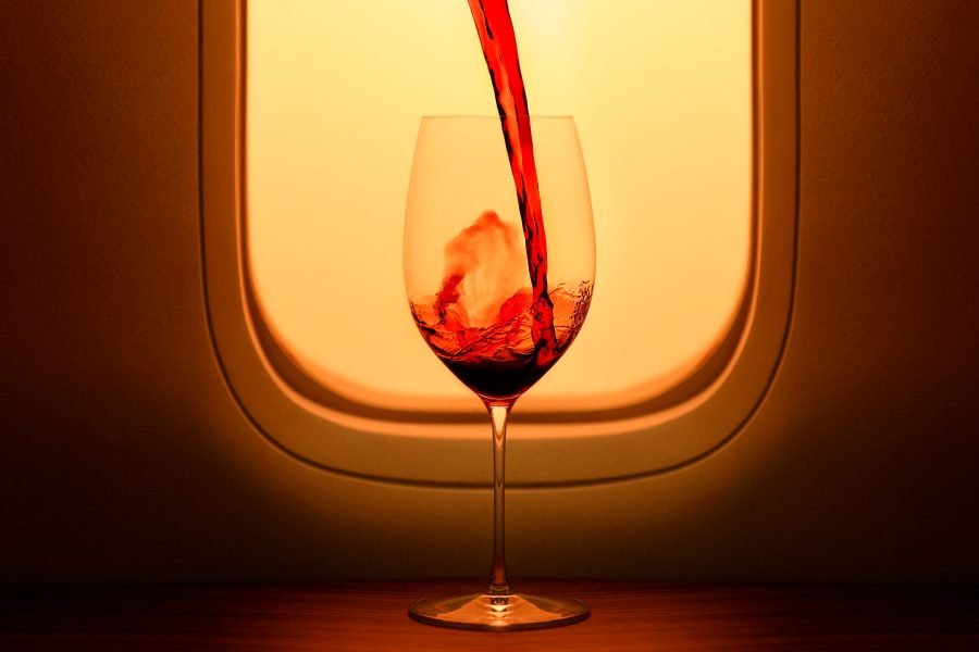 A closeup of red wine being poured into a glass on the ledge of a seat by the aircraft window.